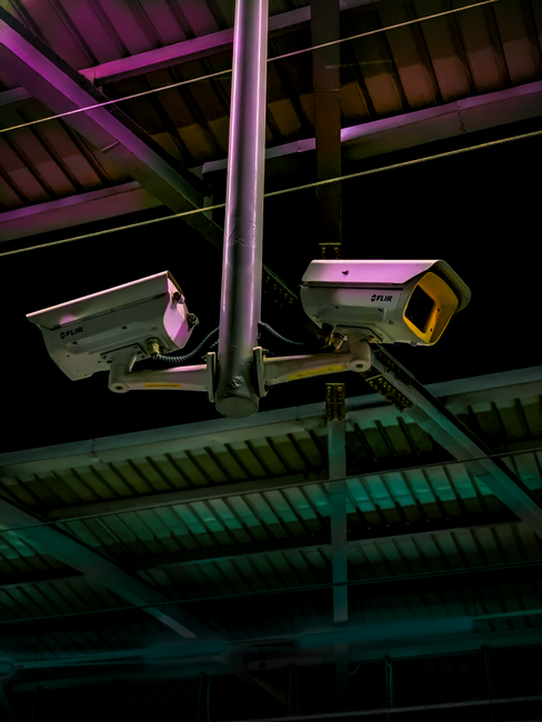 Pair of security cameras installed in an industrial setting with vibrant lighting.